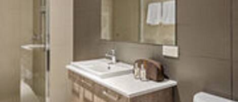A modern bathroom with a large mirror, a sink, and a toilet.