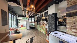 L’intérieur d’un café, avec un plancher en bois, un tableau noir servant de menu et une vitrine où sont exposés des produits alimentaires.