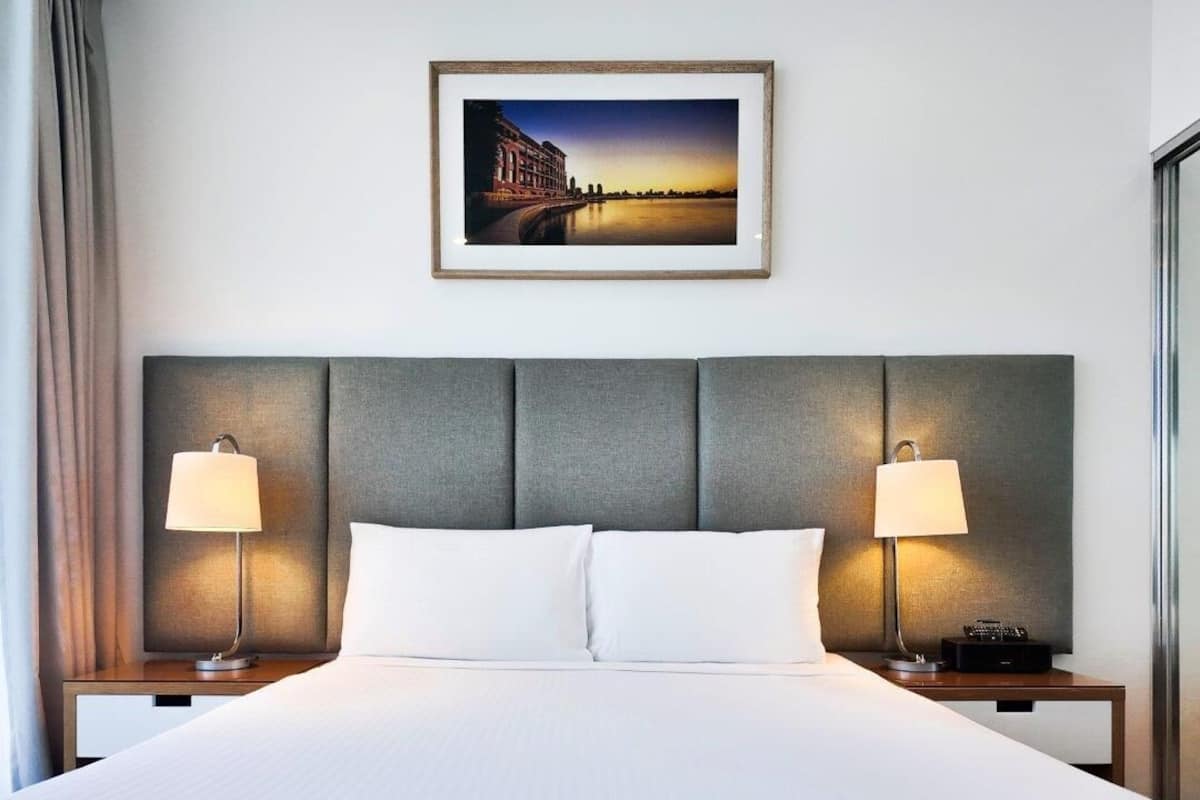 Habitación de hotel con una cama grande, dos lámparas de noche, un cuadro en la pared y un espejo a la derecha.