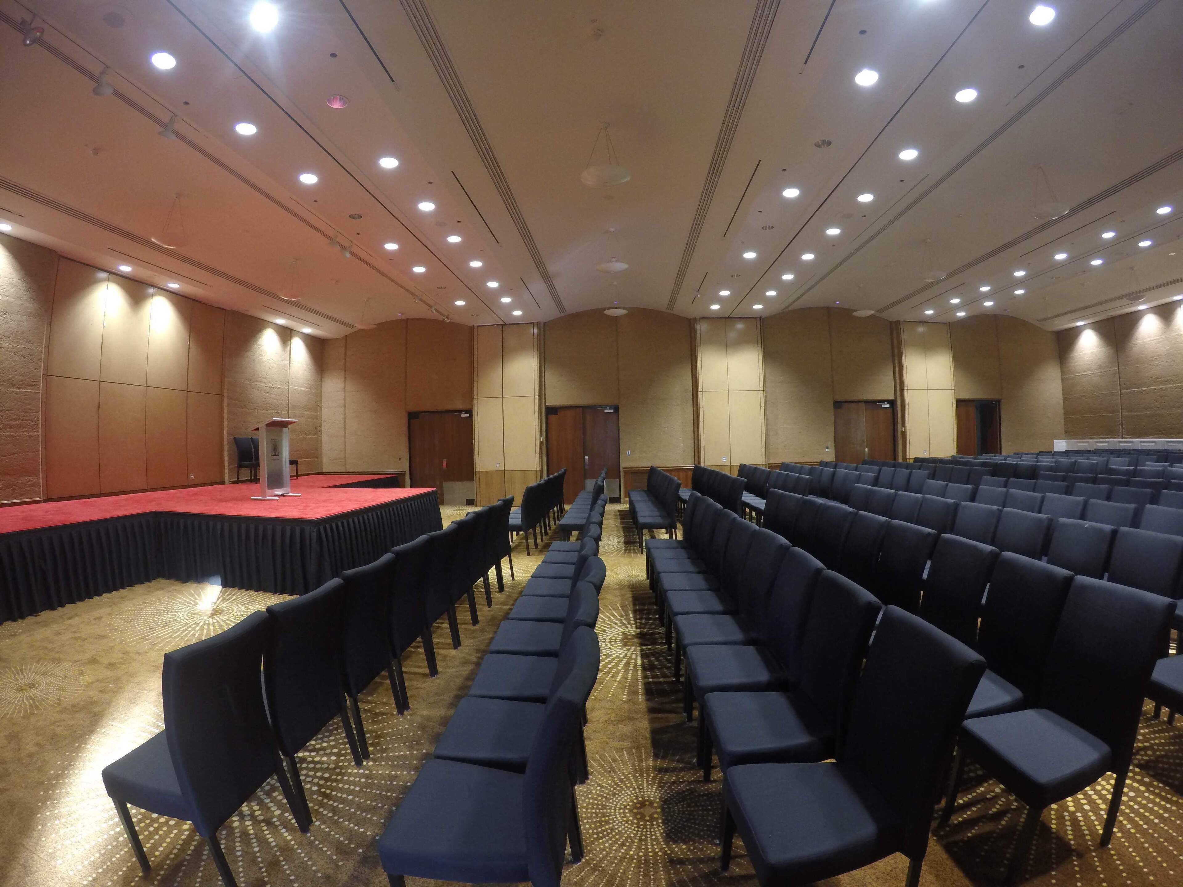 A large conference room with rows of chairs, a stage with a red carpet, and a podium.