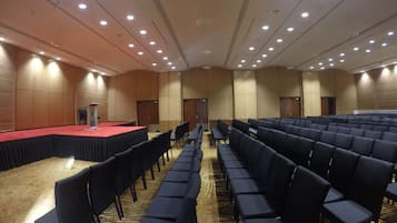 Ein großer Konferenzraum mit Reihen von Stühlen, einer Bühne mit rotem Teppich und einem Rednerpult.