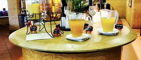 A self-serve juice station with a large dispenser and two pitchers of orange juice.