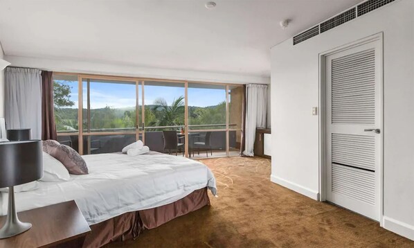 Un dormitorio con una cama grande, un escritorio y un balcón con vistas a la vegetación.