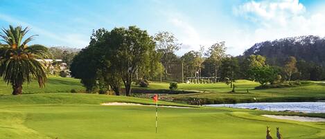 A golf course with a flagstick, water hazards, and a stone wall.