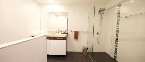 A modern bathroom with a glass shower enclosure, a white vanity with a mirror, and a dark tiled floor.