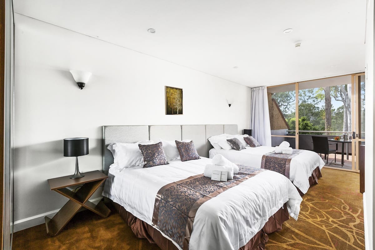 A hotel room with two beds, a desk, and a balcony.