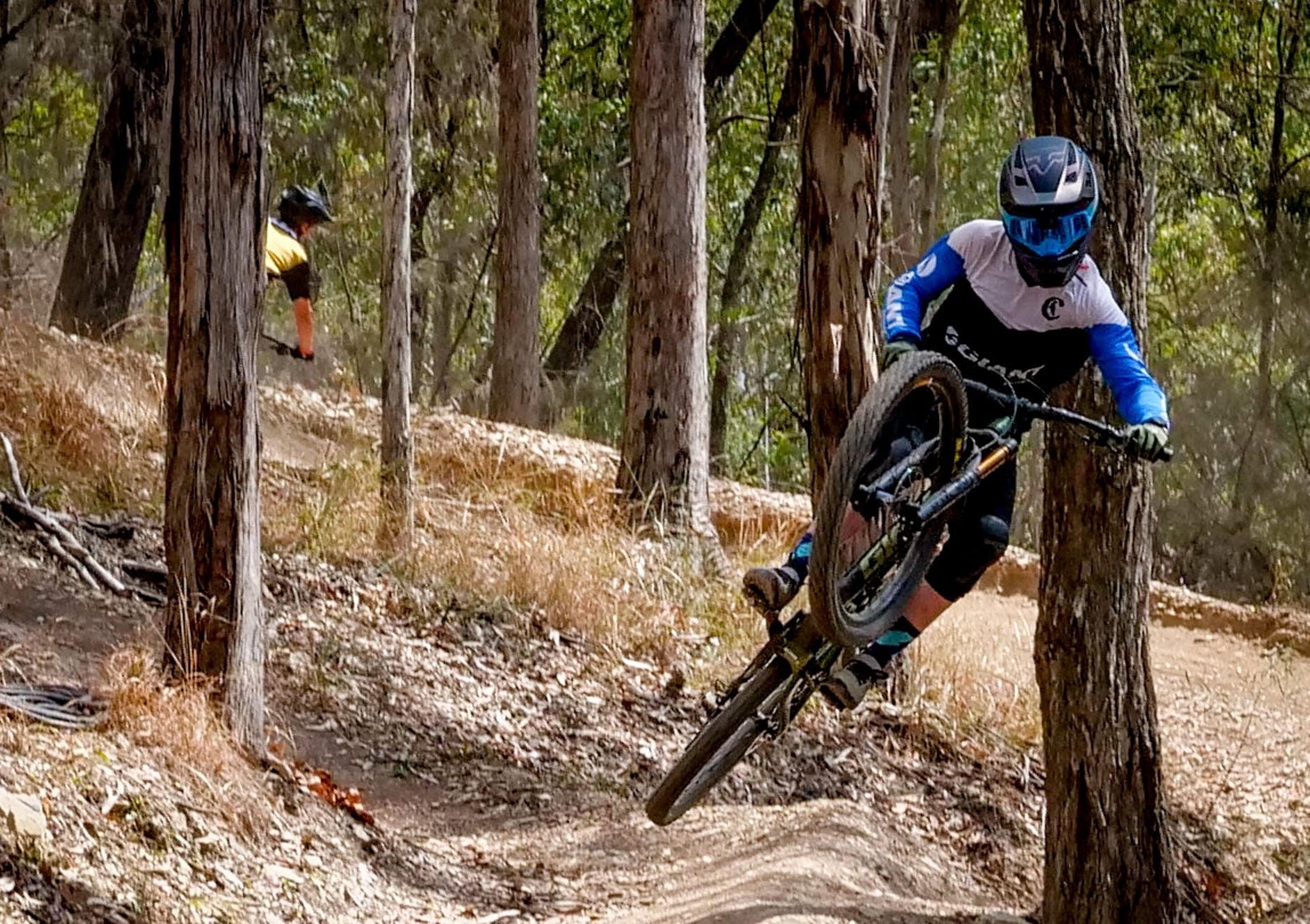 Un ciclista de montaña pedaleando por un sendero de tierra en un área boscosa.