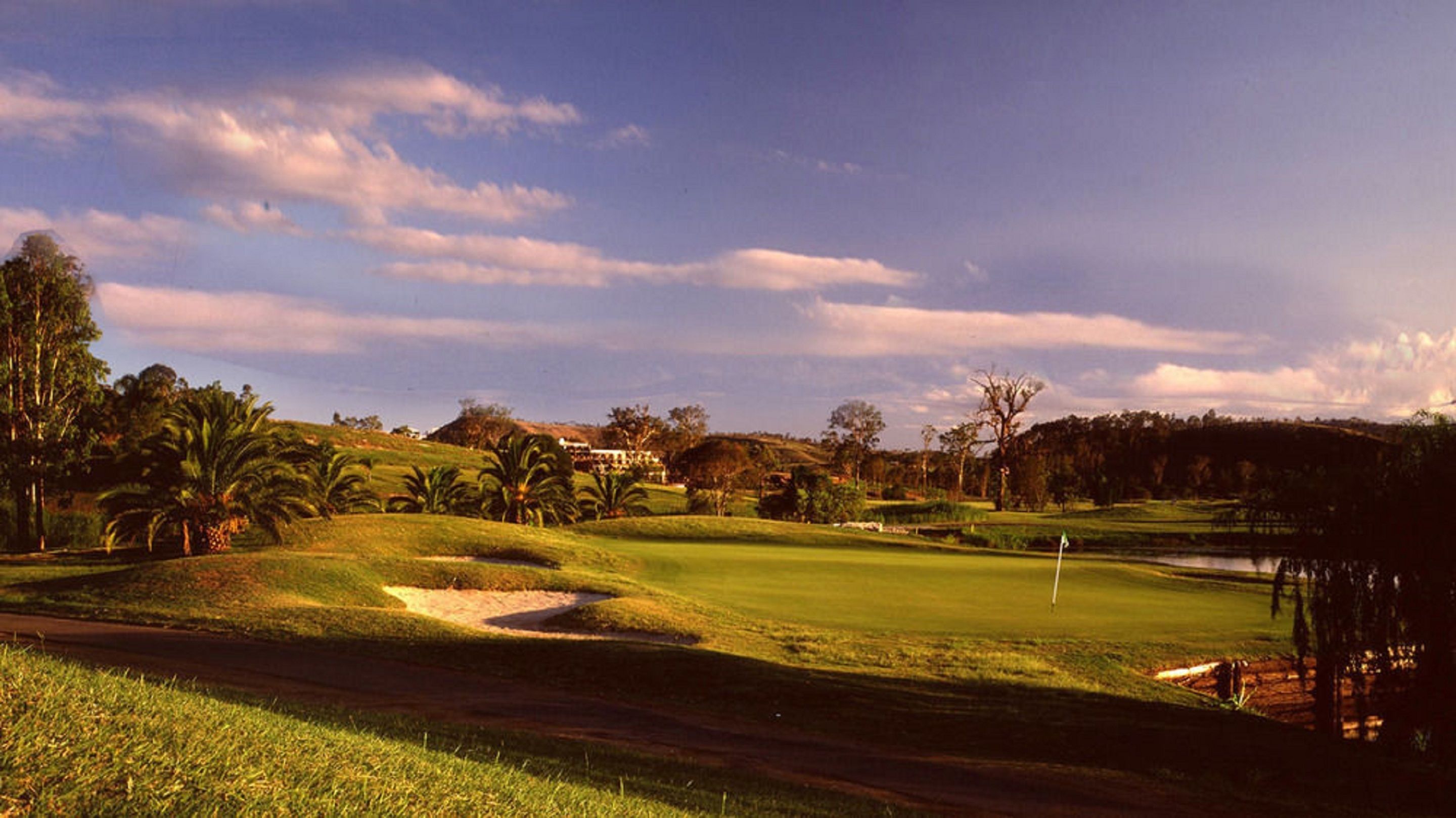 Campo de golf con obstáculo acuático, búnkeres de arena y un mástil con bandera.