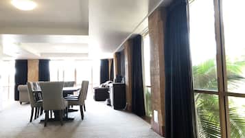 Una habitación de hotel con comedor, ventanas grandes con cortinas y una lámpara en el techo.