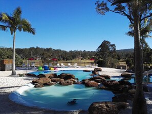 Un área de piscina con rocas, sillas de descanso y palmeras.
