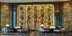 A lobby with a decorative wall, seating area, and two individuals seated at a table. - Wanda Reign Chengdu Hotel (Chengdu)