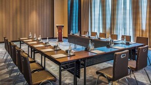 Ein Konferenzraum mit einem langen Tisch, Stühlen, einem Rednerpult und einem großen Fenster mit Vorhängen.