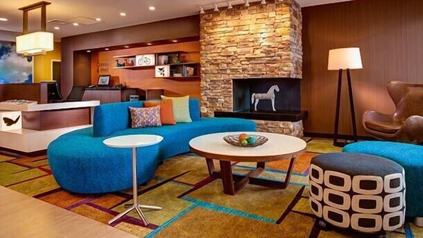 A modern lobby with a stone fireplace, a blue sofa, a round coffee table, and a reception desk. - Fairfield Inn & Suites Utica (Utica)