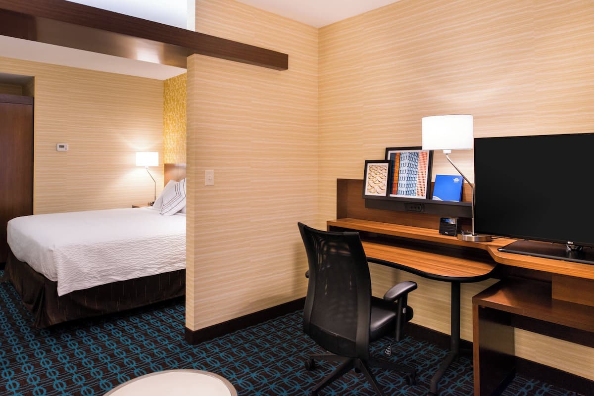 A hotel room with a bed, desk, chair, TV, and a lamp.