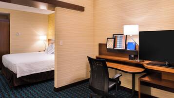 Una habitación de hotel con cama, escritorio, silla, televisor y lámpara.