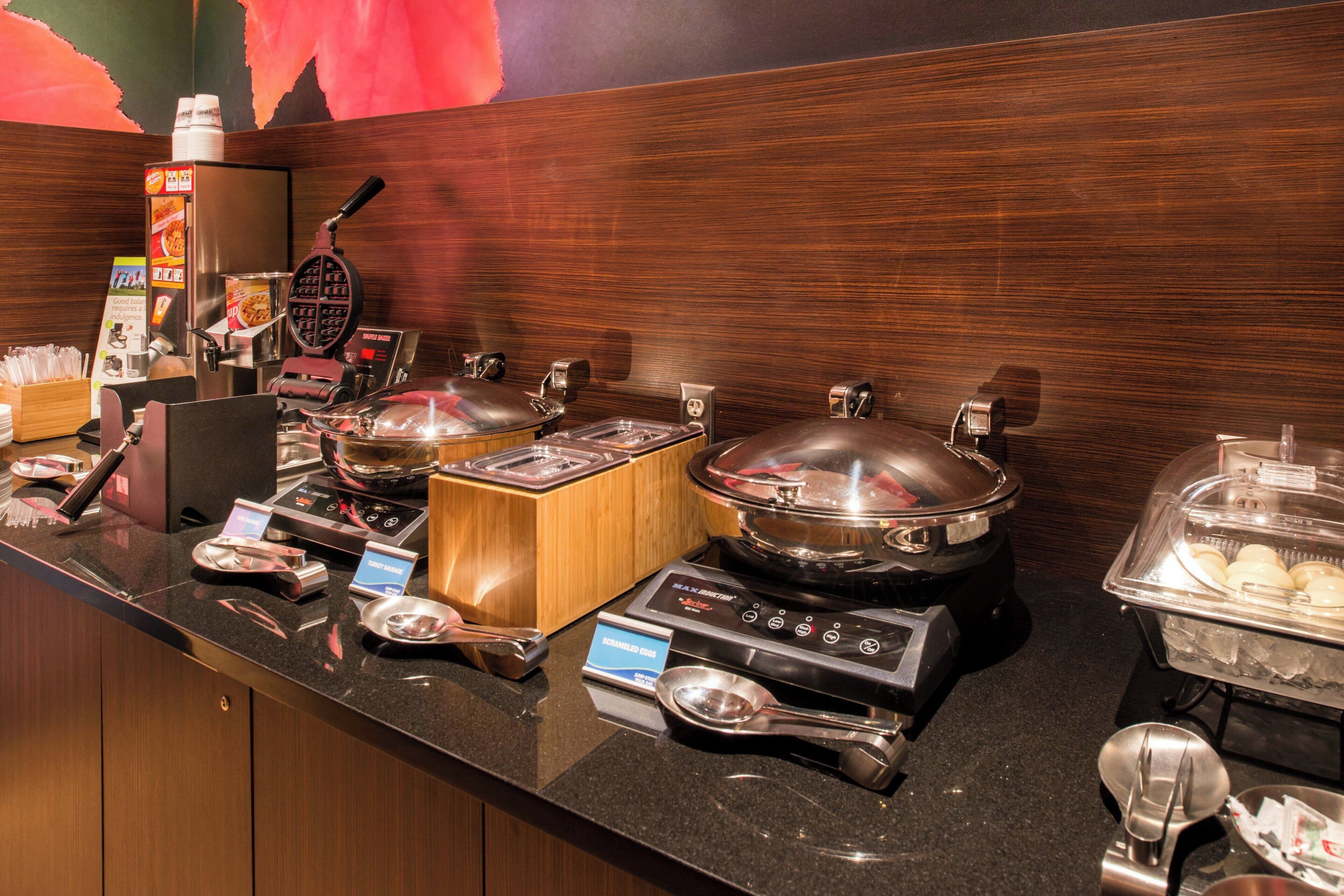 A buffet setup with various food stations, including a waffle maker, hot pots, and a salad bar.