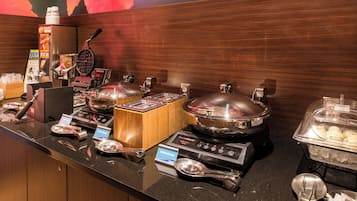 A buffet setup with various food stations, including a waffle maker, hot pots, and a salad bar.