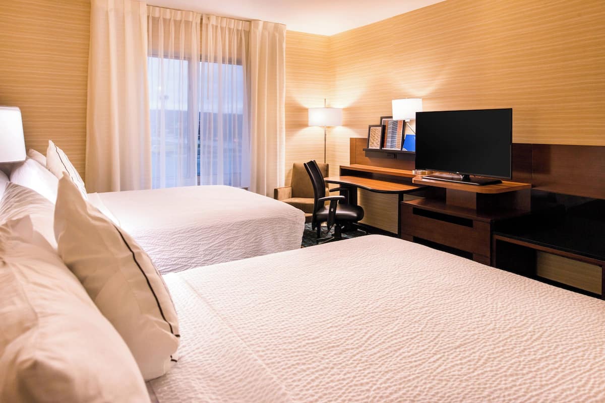 A hotel room with two beds, a desk with a TV, a lamp, and a window with curtains.