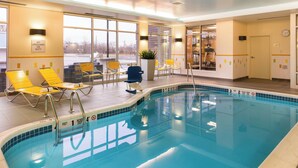 An indoor swimming pool with clear water, yellow lounge chairs, and a view of the outside through large windows. - Fairfield Inn & Suites Utica (Utica)