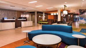 A hotel lobby with a reception desk, blue seating area, and a large painting of a cloudy sky. - Fairfield Inn & Suites Utica (Utica)