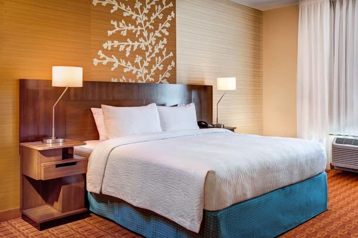 A hotel room with a large bed, two bedside tables with lamps, a decorative wall panel, and a window with curtains.