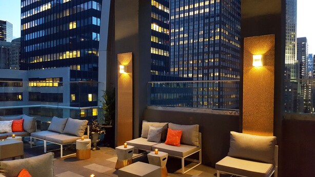 Una terraza en la azotea con mobiliario exterior, vistas de la ciudad e iluminación ambiental.