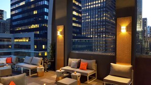 Una terraza en la azotea con mobiliario exterior, vistas de la ciudad e iluminación ambiental.