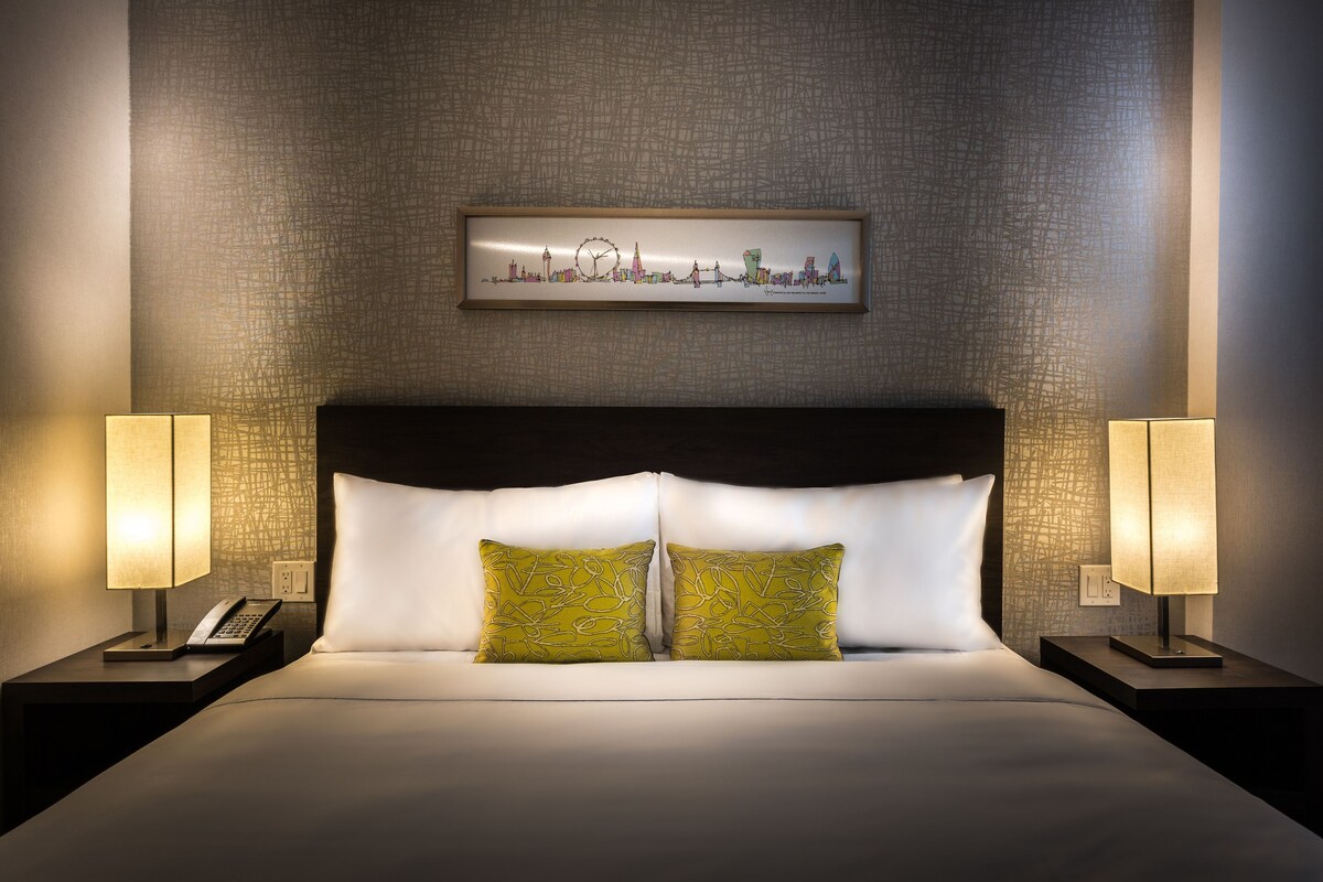 A hotel room with a large bed, two nightstands, a cityscape artwork on the wall, and a textured wall.