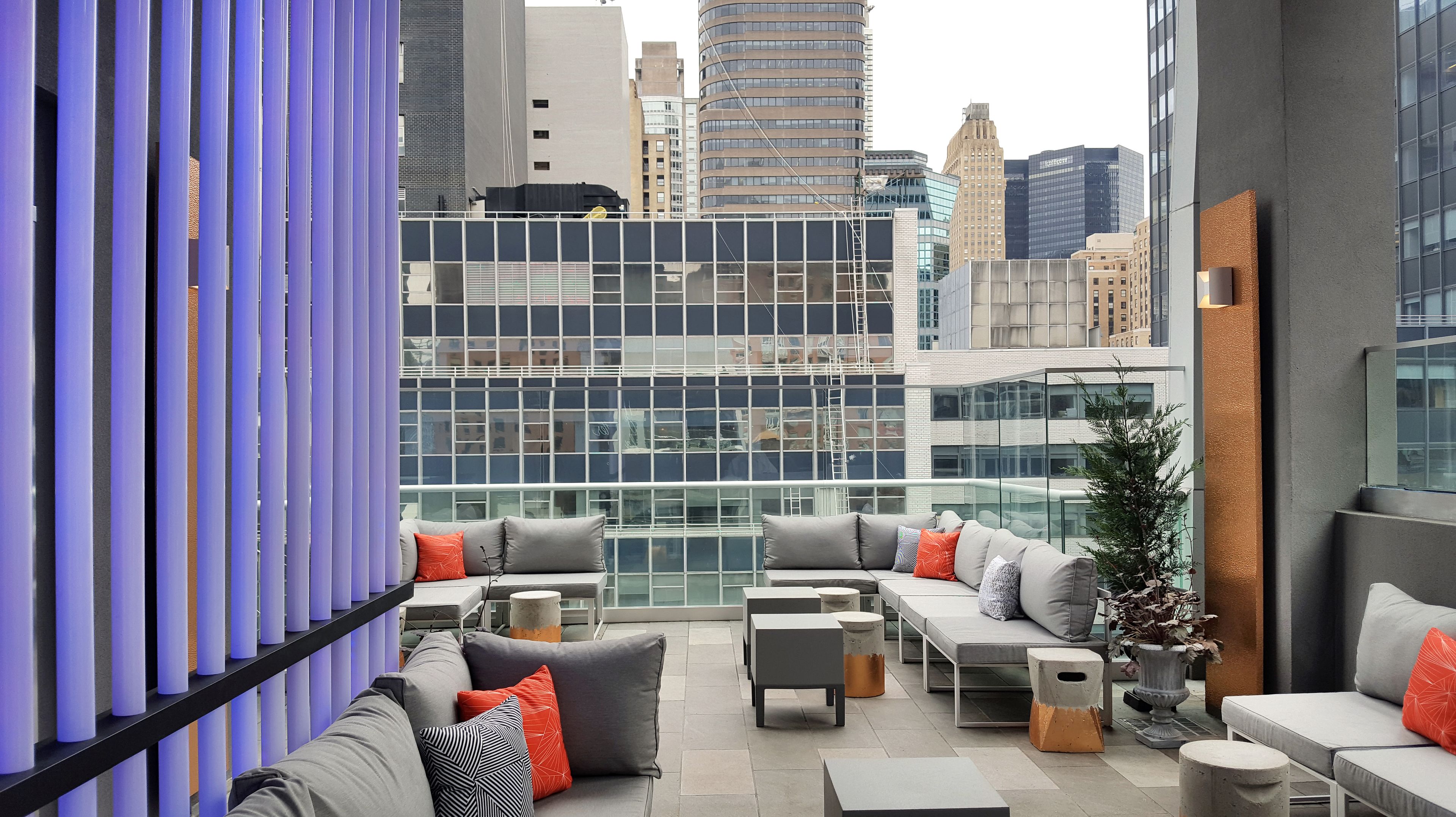 Un lounge en la azotea con asientos modernos, barandilla de cristal y vistas a la ciudad.