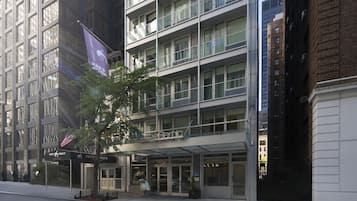 Um hotel com vários andares, fachada de vidro, uma bandeira e uma placa indicando bar e restaurante.