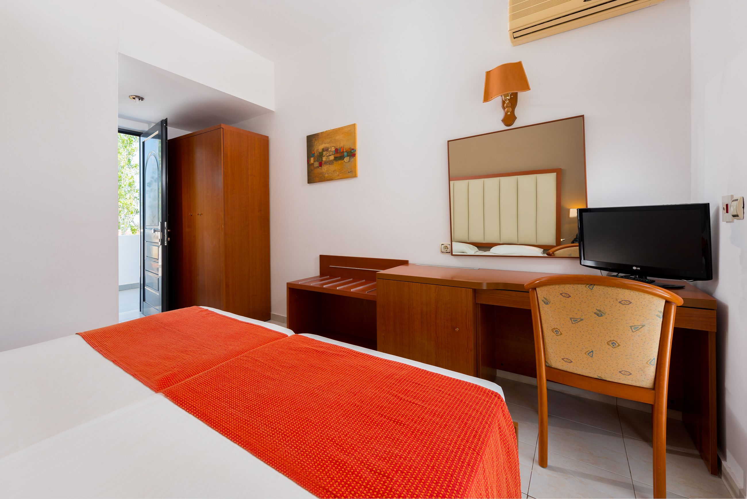 A hotel room with a bed, a desk, a chair, a television, a wardrobe, and a painting on the wall.