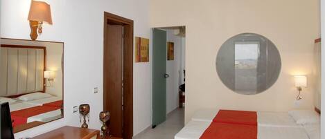 Quarto de hotel com cama, escrivaninha, cadeira, televisão e espelho.