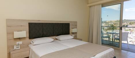 Una camera d'albergo con un letto grande, un telefono sul comodino e vista sulla città tramite una porta in vetro.