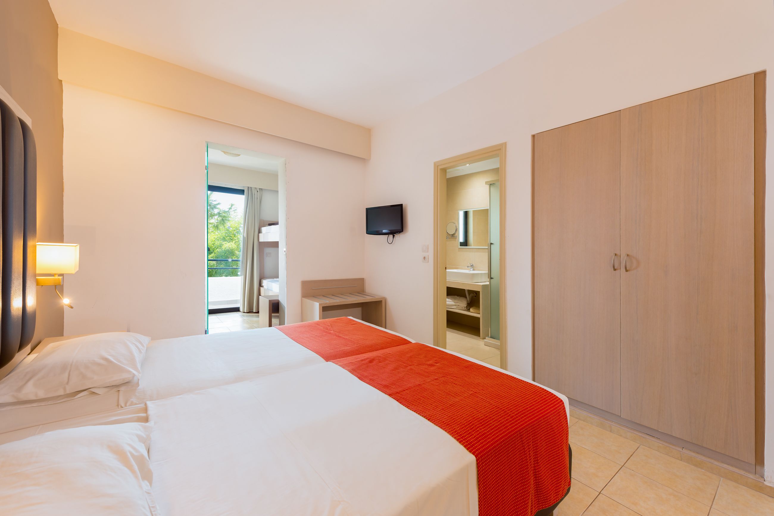 A hotel room with two beds, a TV, a wardrobe, and a bathroom visible through an open door.