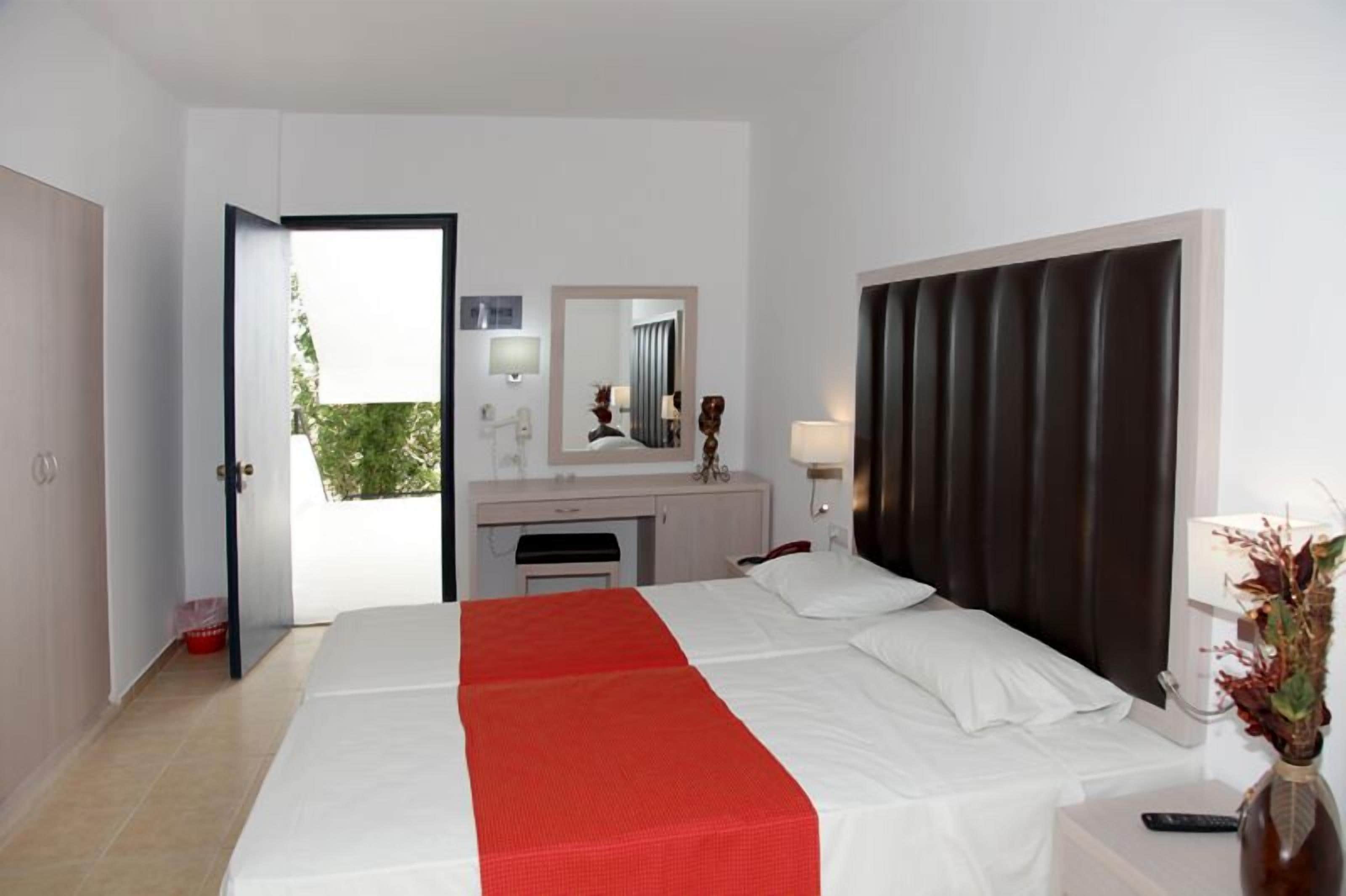 Une chambre d’hôtel avec un lit, un bureau, un miroir, une fenêtre et une porte.