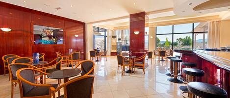A spacious restaurant with wooden chairs and tables, a bar area, and large windows offering a view.