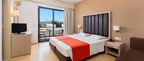 A hotel room with a large bed, a desk with a TV, a bedside table with a phone, and a view of the outdoors through a sliding door.