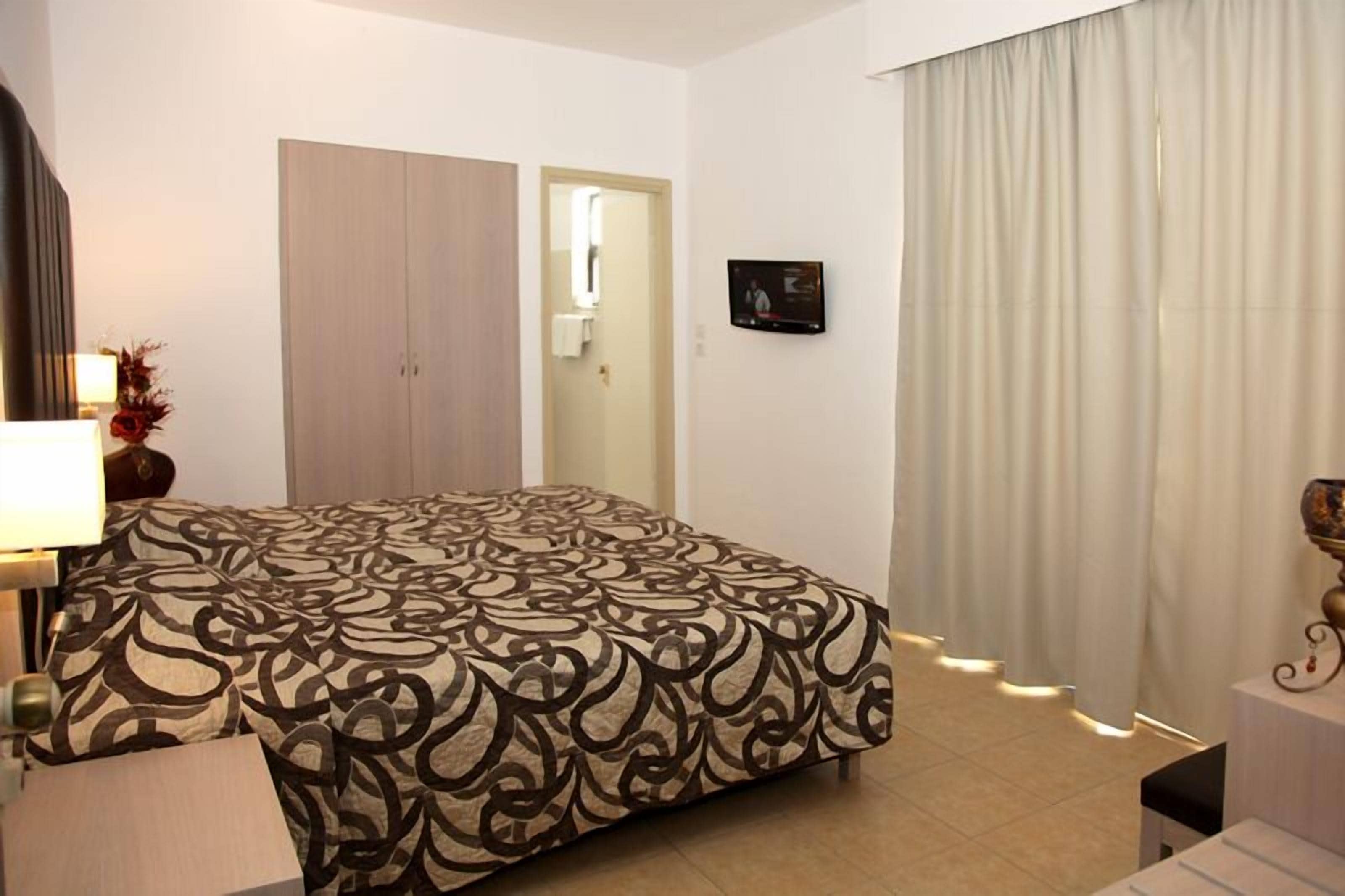 A hotel room with a bed, a wardrobe, a TV, and a window with curtains.