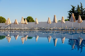 A pool with umbrellas and lounge chairs, reflecting in the water.
