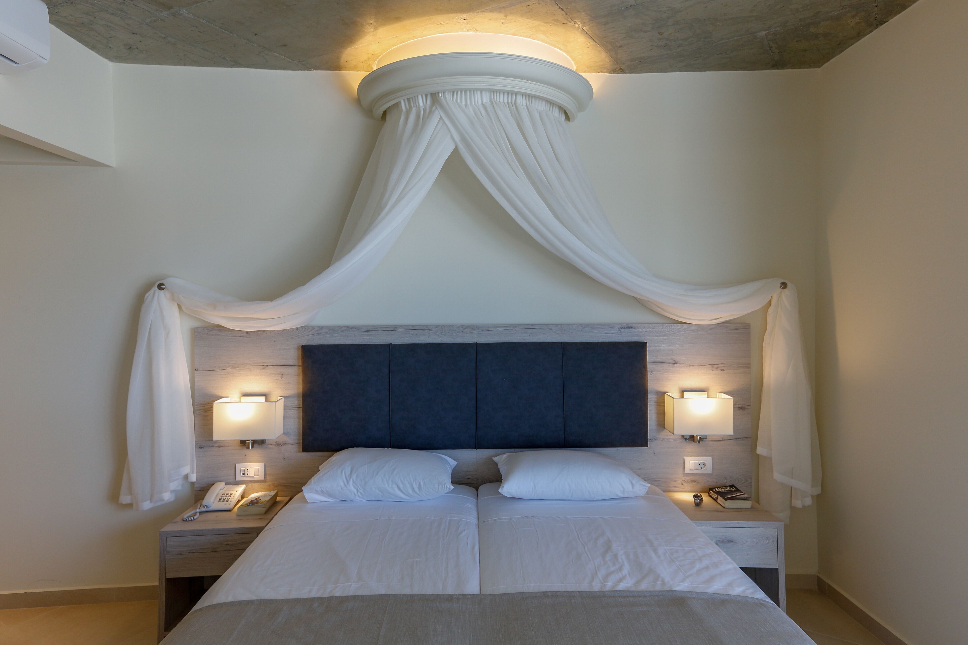 Un lit double avec une tête de lit sombre, deux tables de chevet avec des lampes et un baldaquin au-dessus.