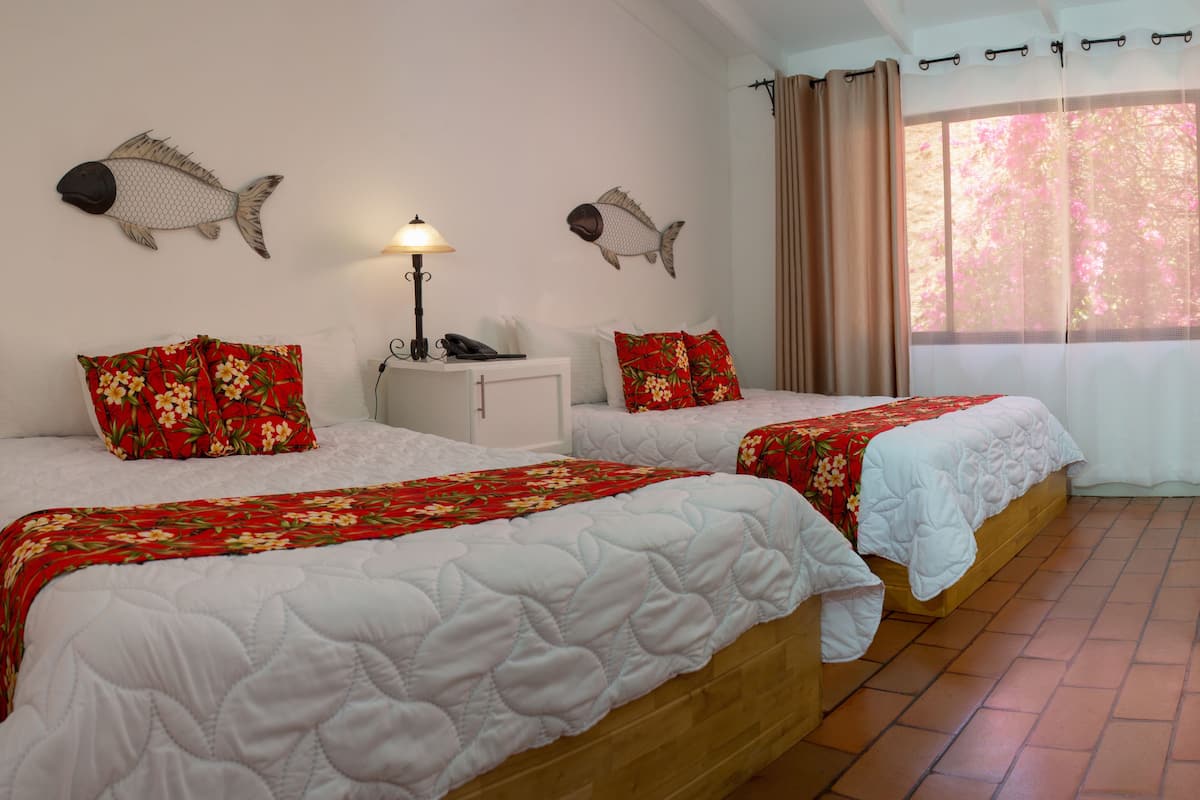 A hotel room with two beds, a bedside table with a lamp, a TV mounted on the wall, and a window with curtains.