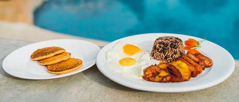Two plates of breakfast food on a table by a pool.