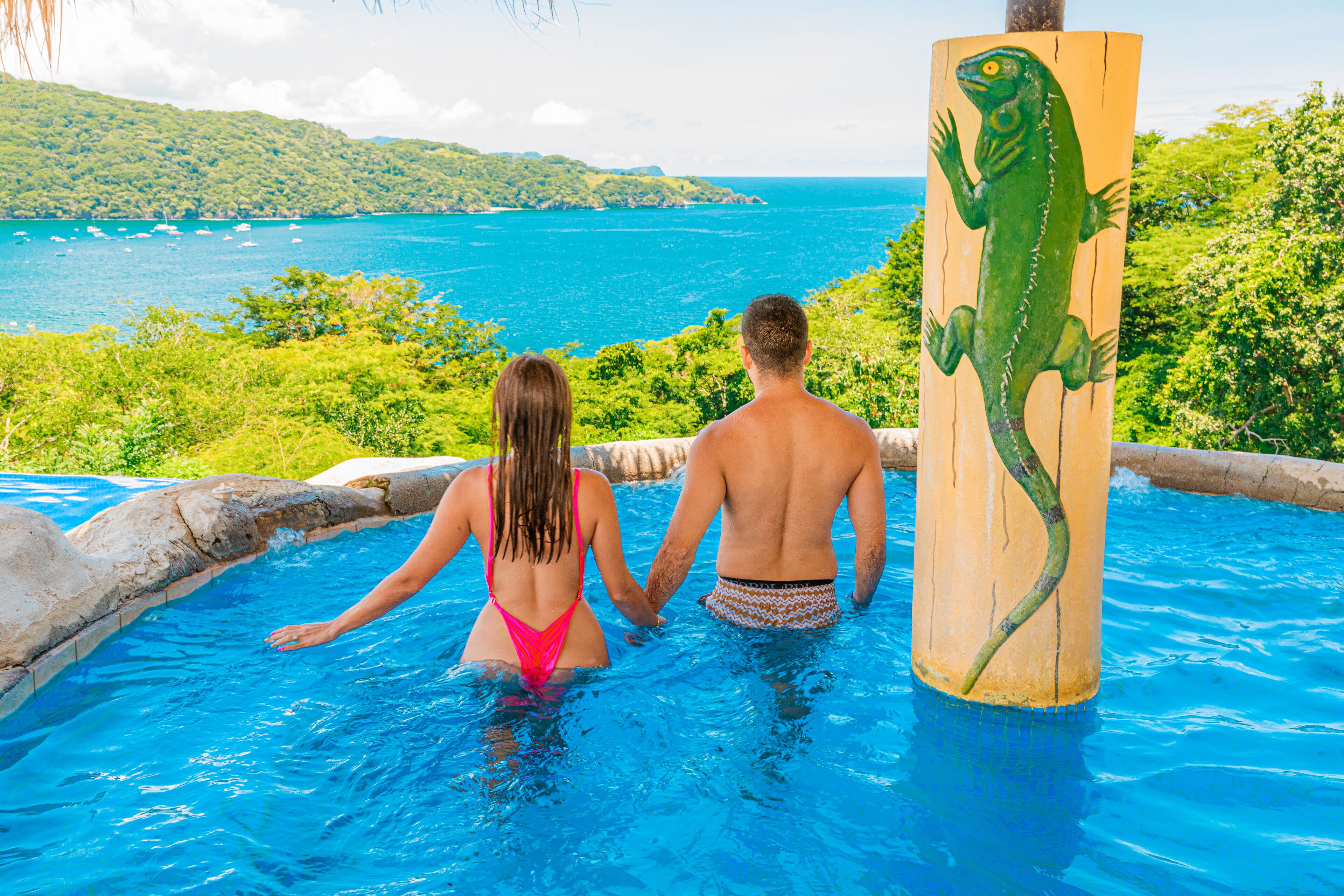 Um casal em uma piscina com vista para a paisagem costeira.