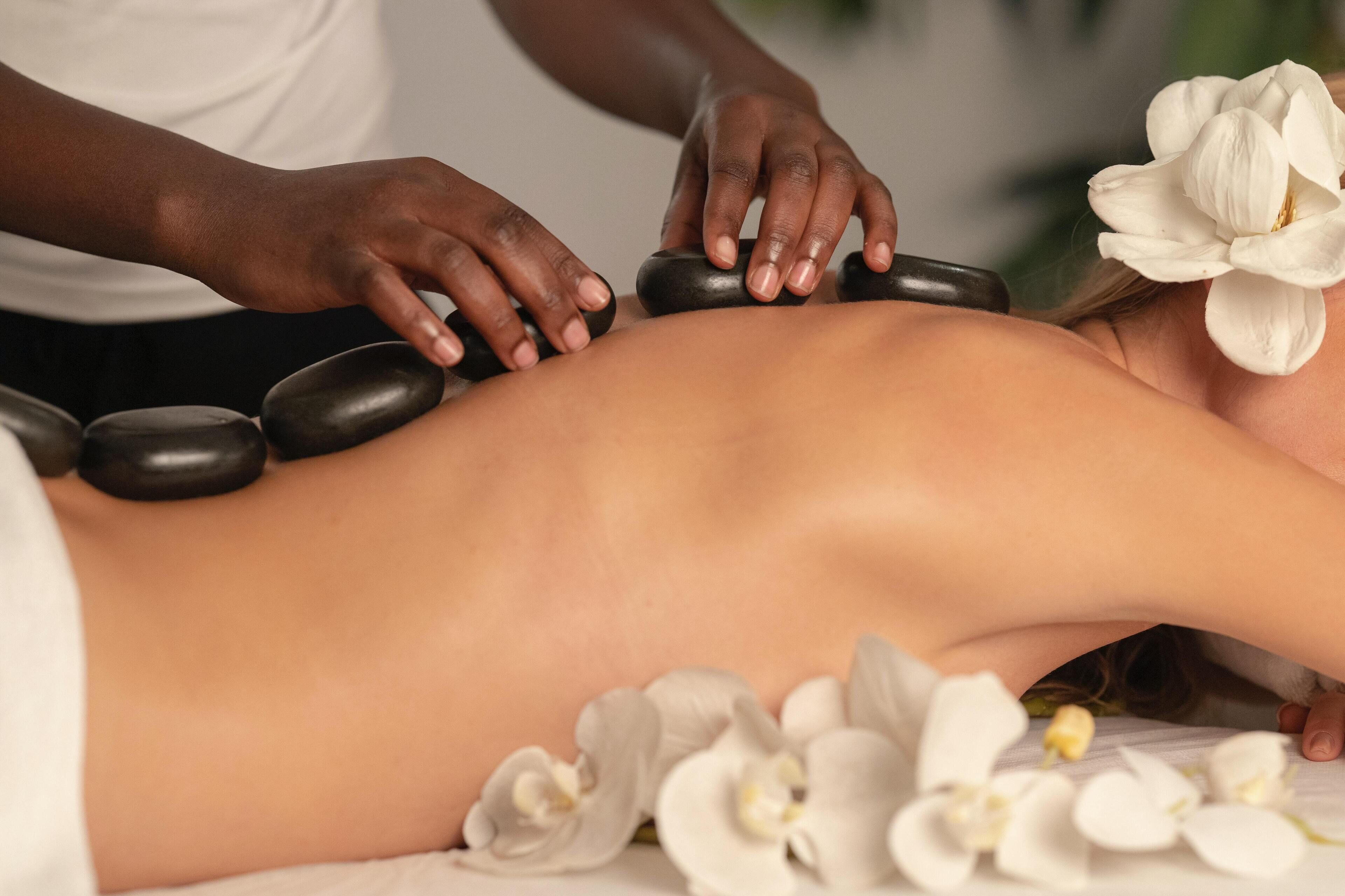 Een persoon ontvangt een massage met stenen en witte bloemen op een massagetafel.