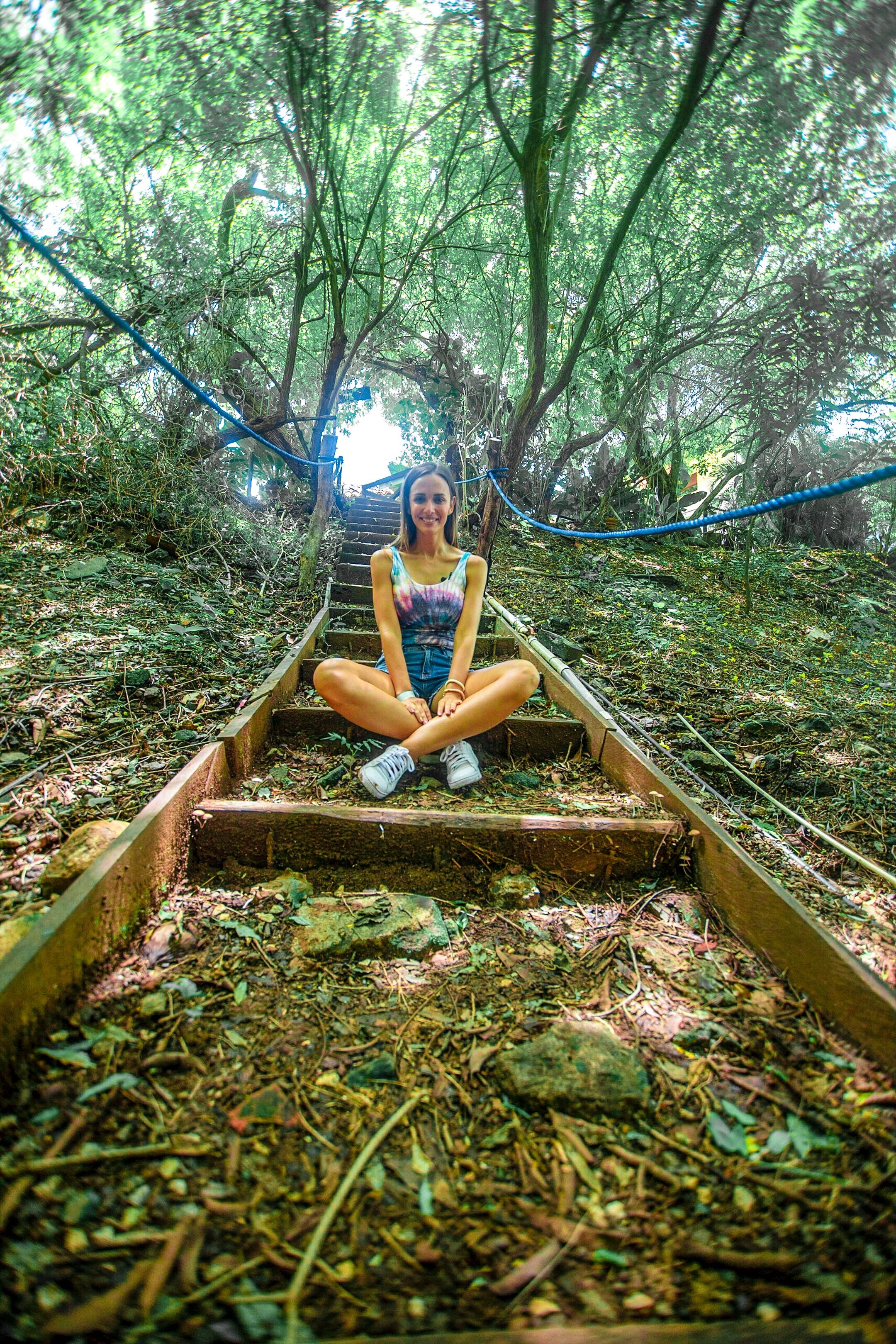 A person sitting on a wooden staircase surrounded by dense foliage.