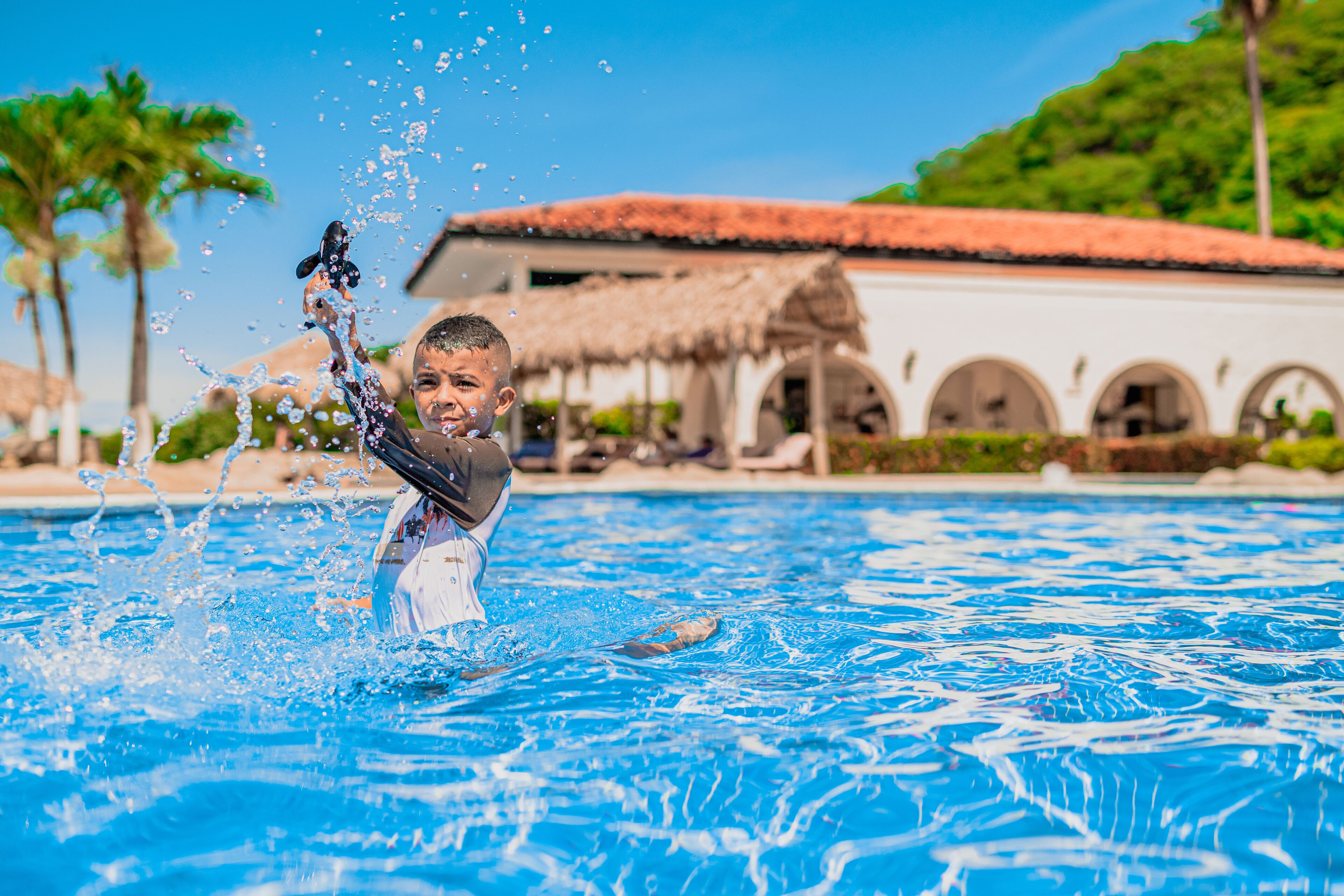A pool with clear blue water, a person in the water, and a building with arches in the background.