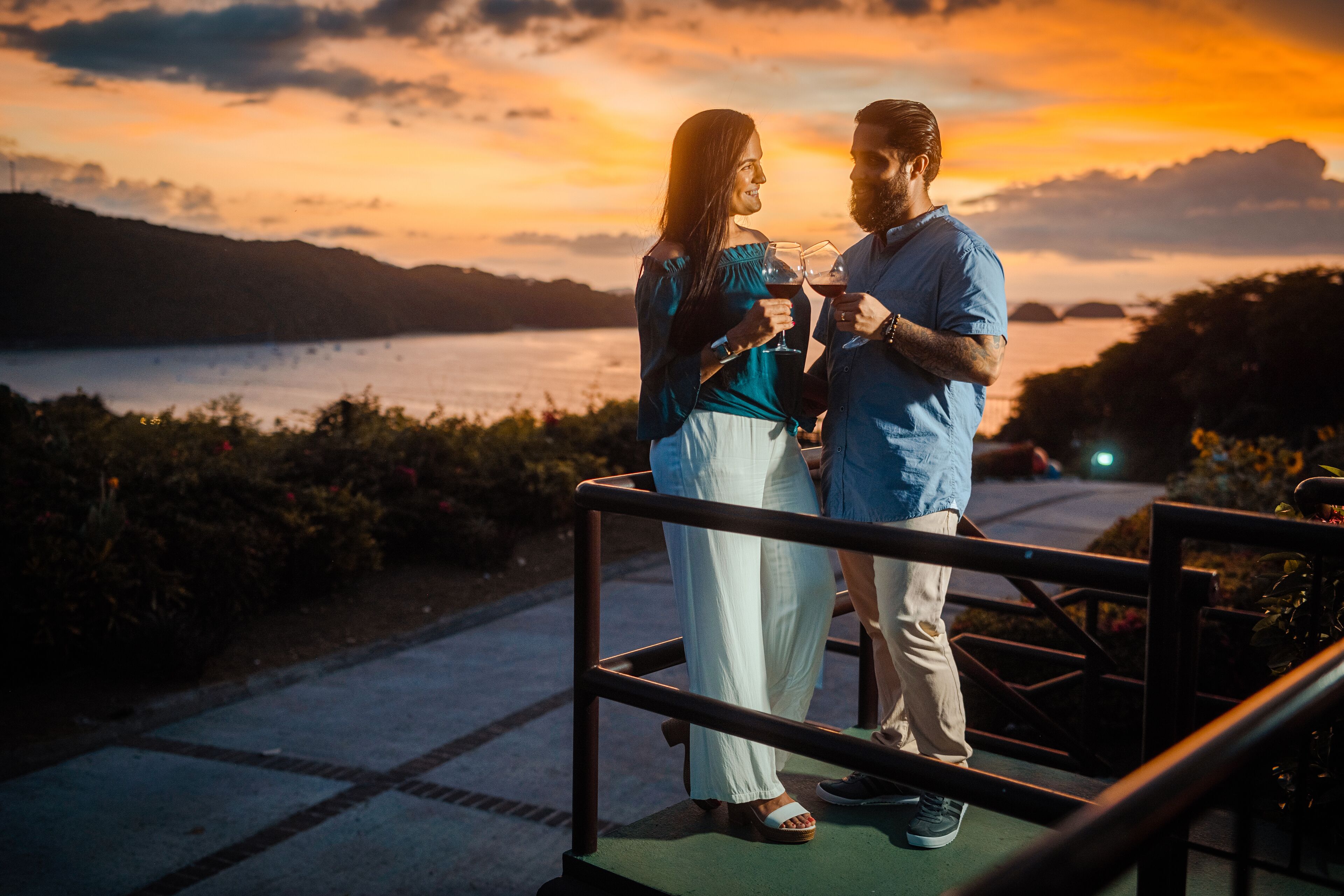 A couple standing on a balcony with a scenic view of a lake and sunset.