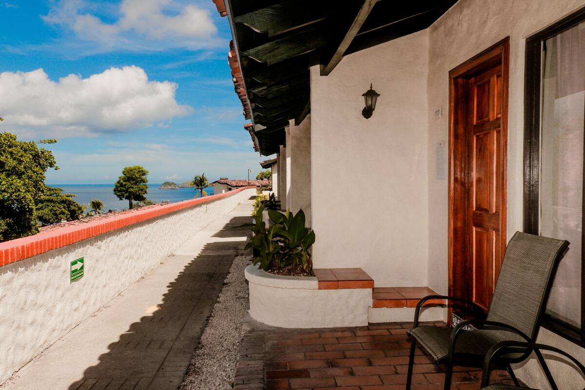 A hotel balcony with a view of the sea, a red railing, and a chair.