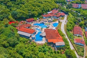 Vista aérea de un complejo turístico con varias piscinas, edificios de techos rojos y abundante vegetación.