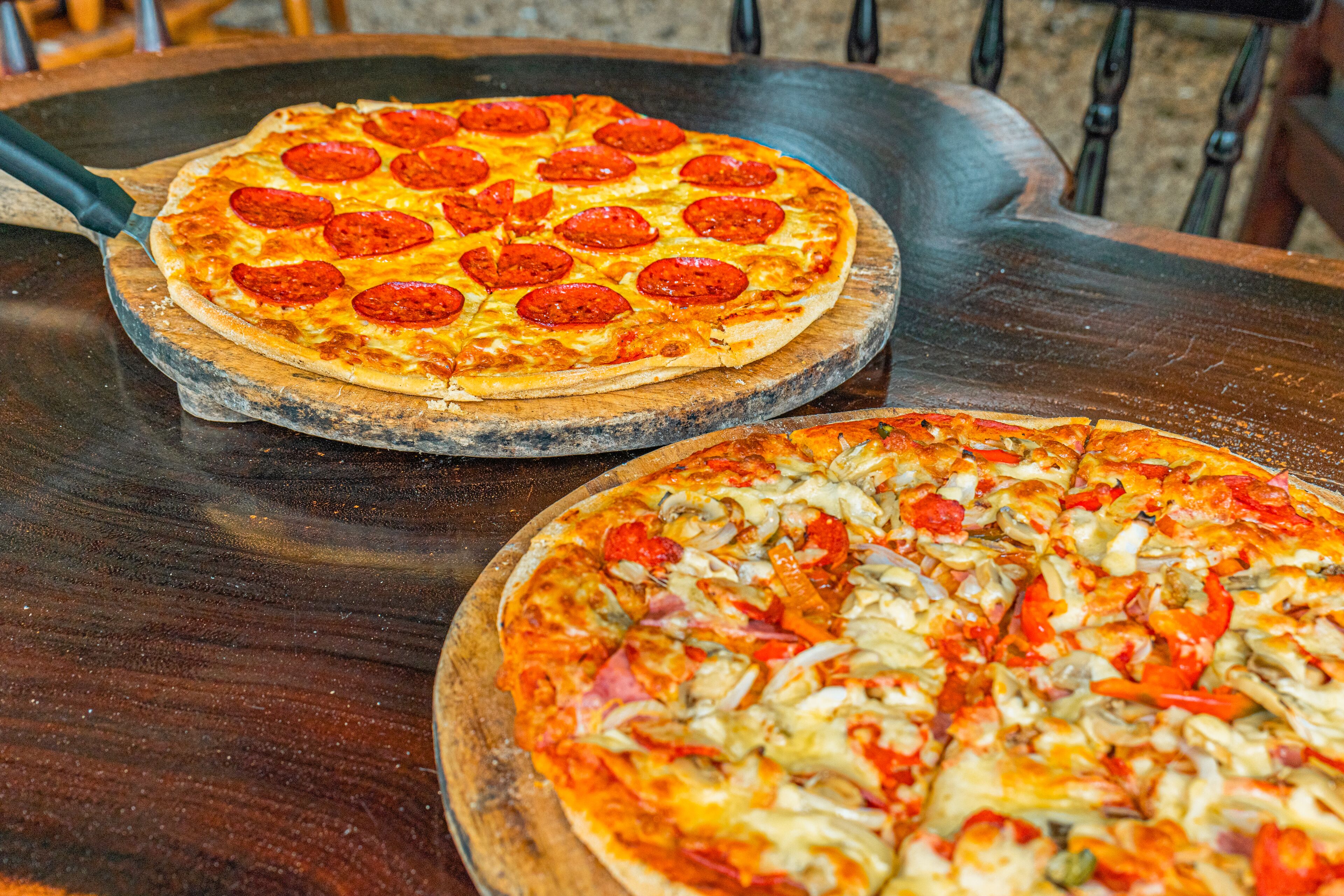 Two pizzas on wooden boards.